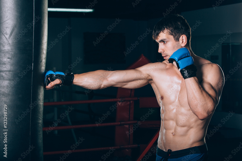 Young Male boxer using a punching bag in gym.