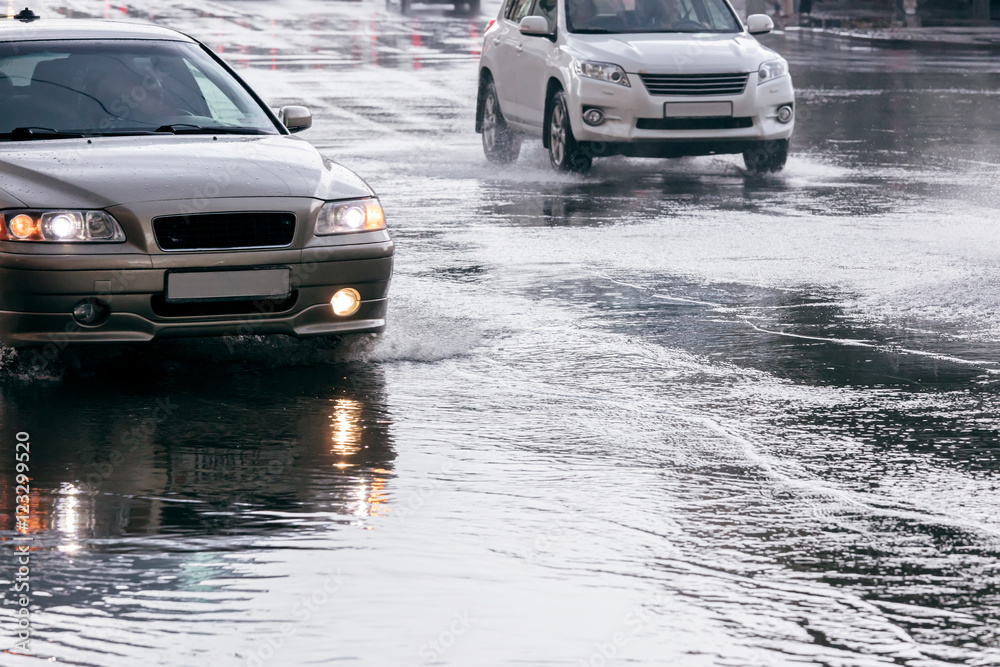 city road flooded with rain water. cars driving on water puddles after downpour. city road flooded with rain water. cars driving on water puddles after downpour.