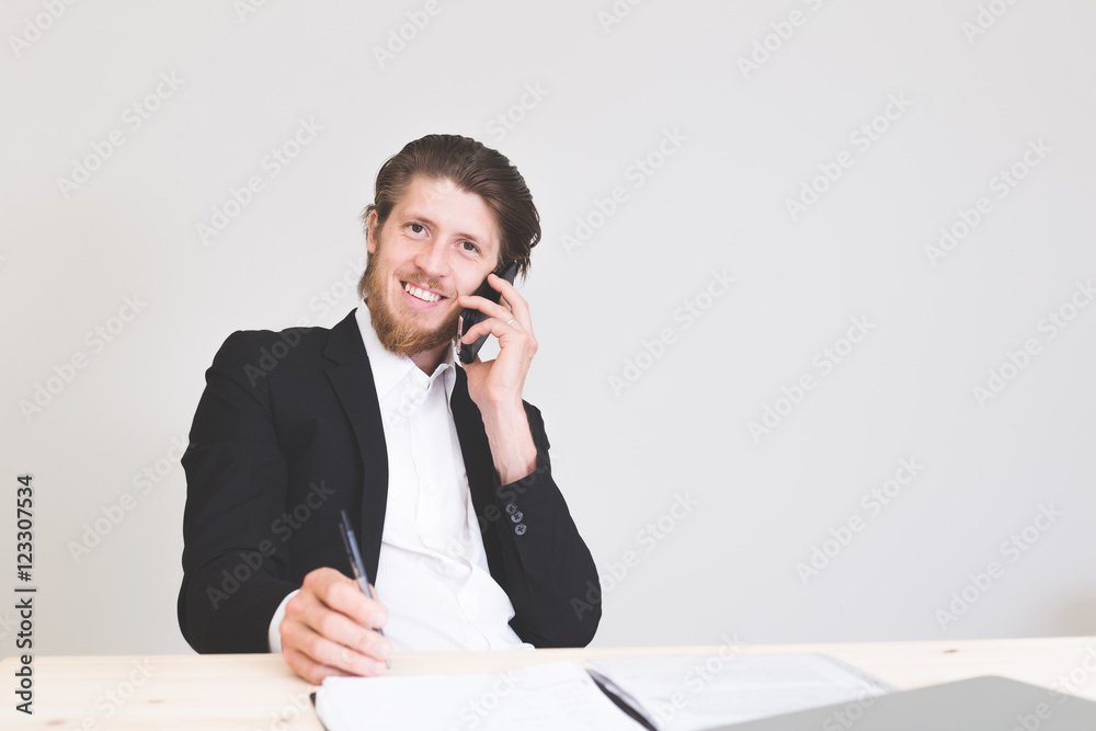 portrait of smiling male employee answering on phone while signing documents at office portrait of smiling male employee answering on phone while signing documents at office