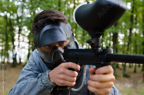 Man attentive with paintball gun wearing protection helmet and d