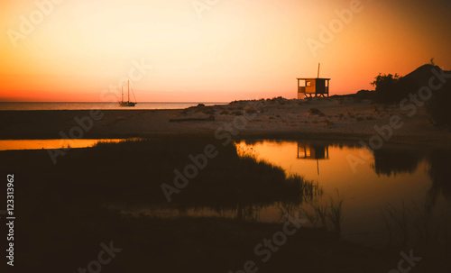 Fototapeta Naklejka Na Ścianę i Meble -  The Sunset over Ostricony Beach (Corsica, France) with Watchtower and Sailing Boat