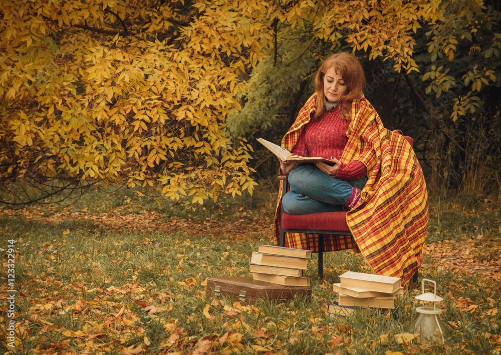 Woman sitting in the autumn park and read book with fall leaves on background Woman sitting in the autumn park and read book with fall leaves on background