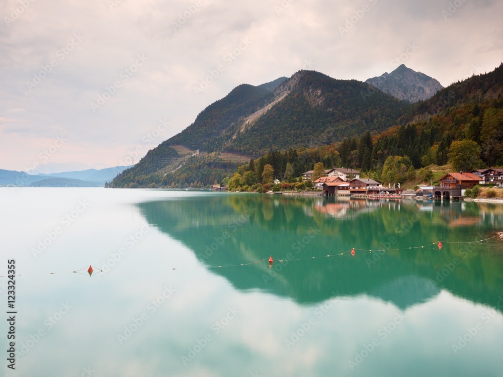 Village on the bank of Alps lake. High mountain peaks in mirror of gren water level.