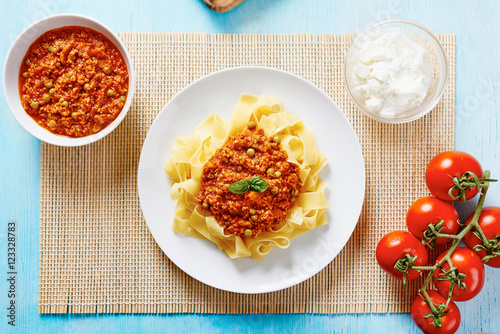 Tagliatelle with Bolognese sauce in white dish surrounded by ricotta cheese, fresh tomatoes, Bolognese sauce in a white bowl on blue table