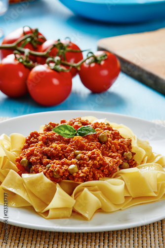 Tagliatelle with Bolognese sauce in white dish surrounded by fresh tomatoes on blue table