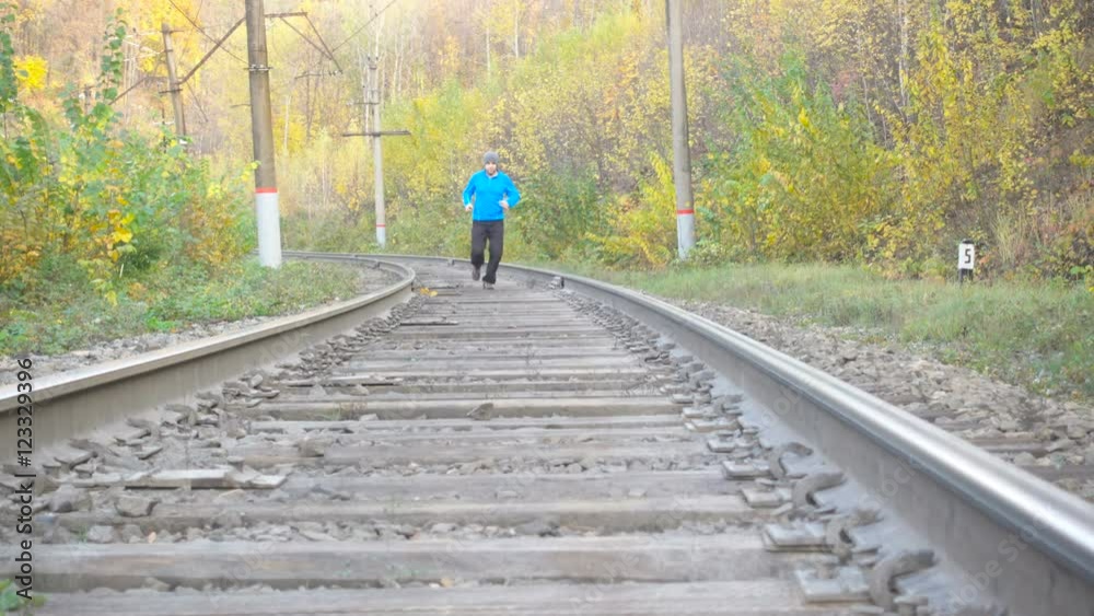 Man Jogging Train Tracks Railway in Autumn Season in forest. Training and exercising outdoors when cross country running in inspirational autumn landscape. Sports Motivation. Man Jogging Train Tracks Railway in Autumn Season in forest. Training and exercising outdoors when cross country running in inspirational autumn landscape. Sports Motivation.