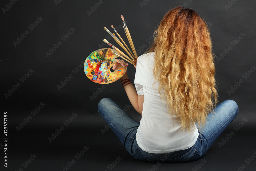 Fototapeta premium Girl painter with a palette and brushes on a dark background. 