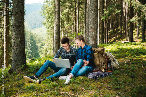 A guy and a girl tourists relax in the mountain forest, sitting and looking at laptop