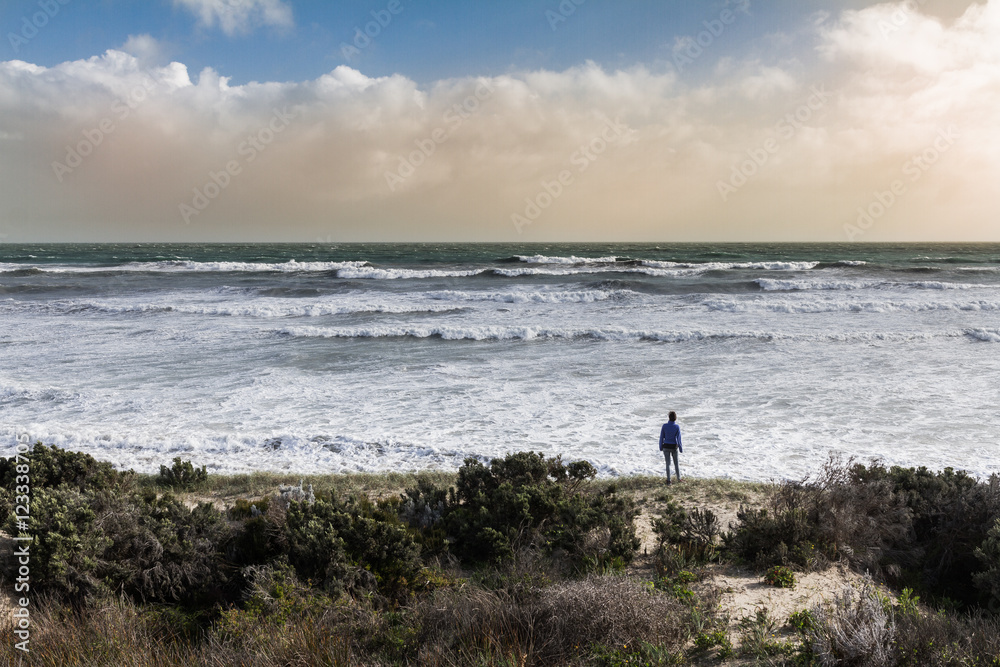 Woman stands in front of ocean with storm in background in Australia