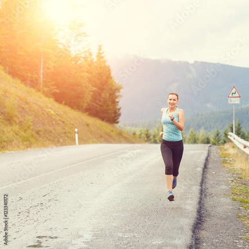 Young athletic woman jogging on road in mountains