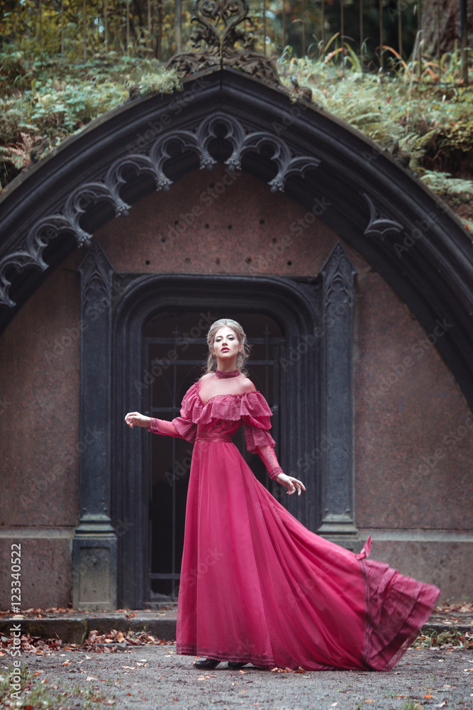 Beautiful woman in vintage burgundy dress with flying train on a background of a Gothic arch.