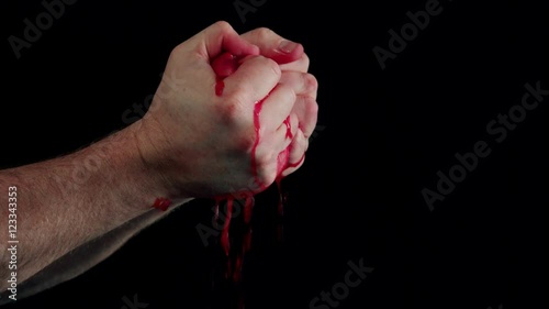 Male hands mashing juicy pomegranate with juices dripping aganst black BG photo