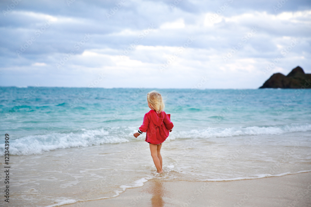 Little girl in red coat running into the water on the beach Little girl in red coat running into the water on the beach