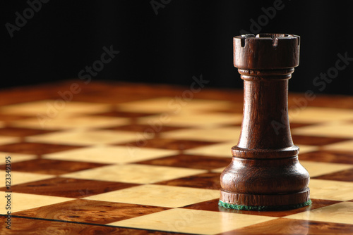 Photography Carved wooden black rook castle chess piece on elegant maple chessboard with dra