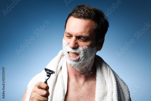 Фотография Man snarling at razor with shaving cream and towel