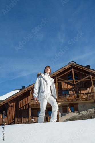 femme se promenant dans la neige devant un chalet en bois