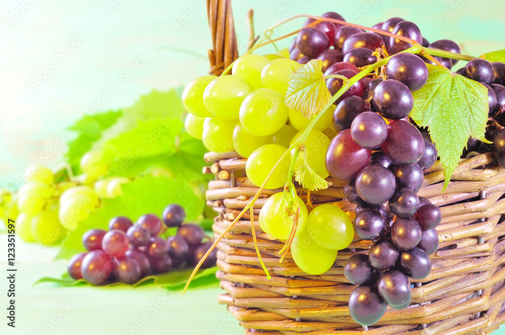 Red and green Grape bunches and leaves in basket on wooden table Red and green Grape bunches and leaves in basket on wooden table
