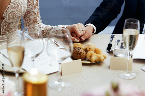 Bride in lace dress holds groom's hand on dinner table