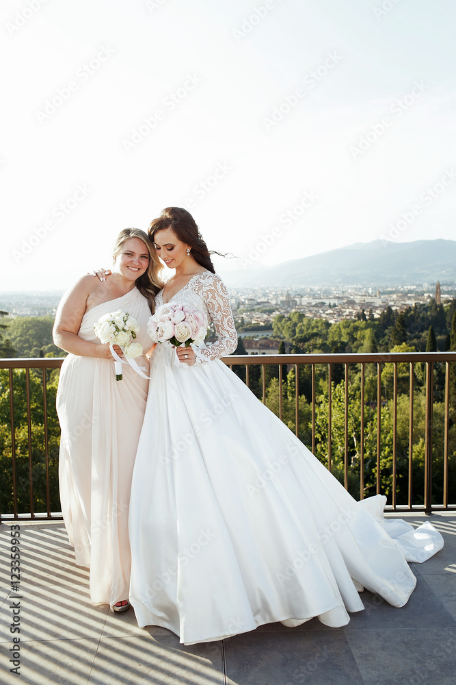 Fototapeta premium Charming bride hugs her bridesmaid tender while they pose on the