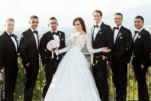 Delightful brunette bride stands between stylish groomsmen in bl