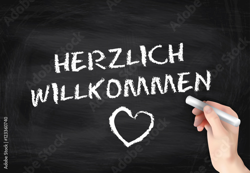 Hand schreibt mit Kreide "Herzlich Willkommen" auf schwarze Tafe