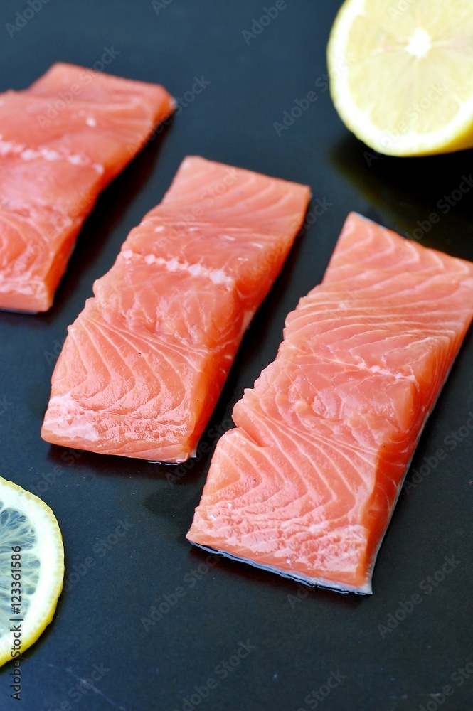 Raw salmon fillet with yellow lemon on black background
