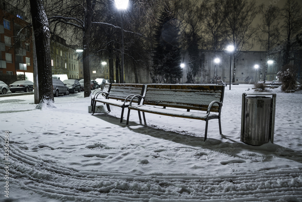 Benches covered in snow at eerily empty playground at night