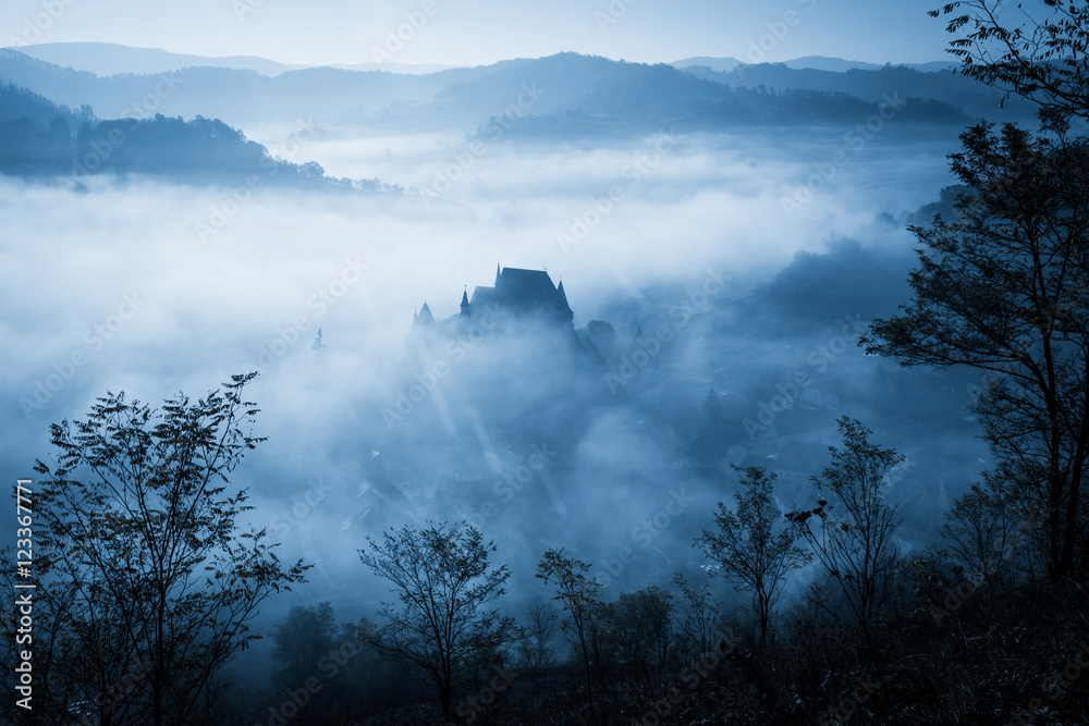 Mysterious misty morning over Biertan village, Transylvania, Romania. Blue colors. spooky, Halloween concept