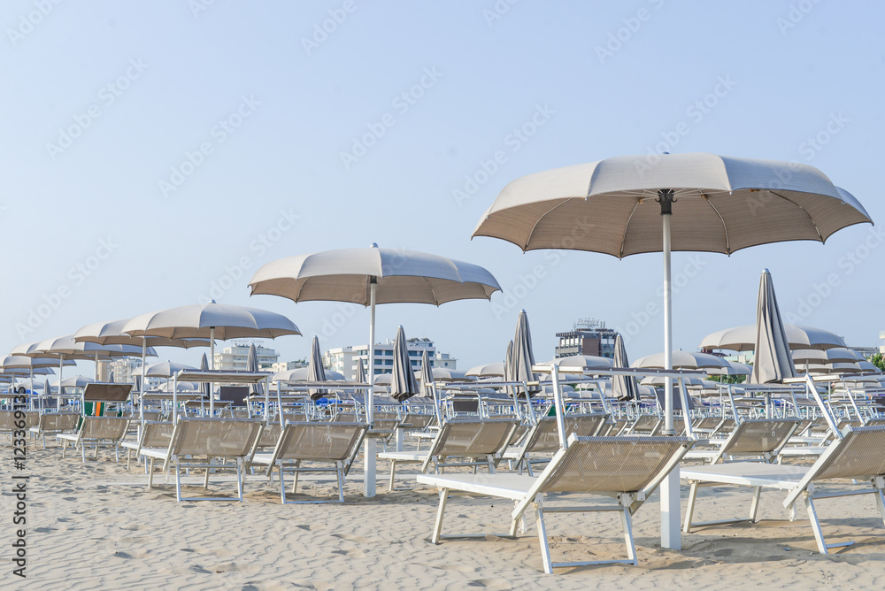 Light sunbeds, loungers and beach umbrellas on empty sand beach