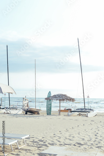 Sea view: sunshade, surf and boats silhouettes on sunset sky, calm resort evening