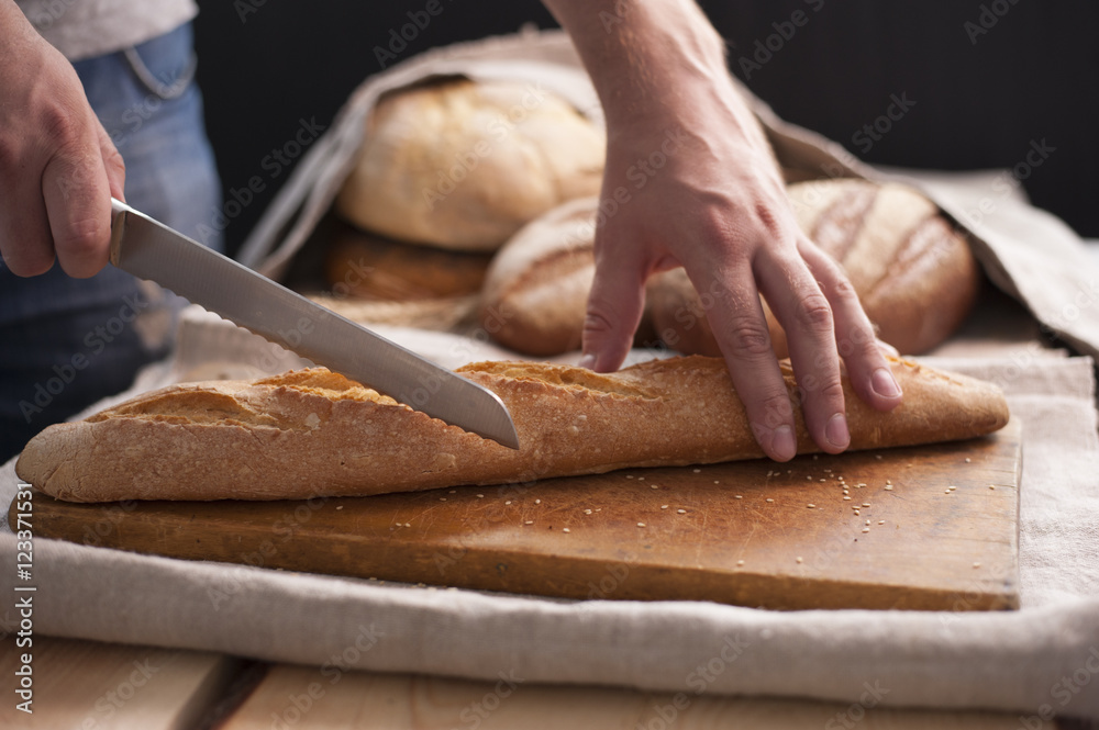 hands cuts baguette on table