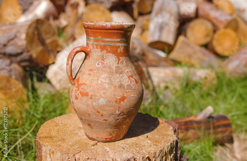 Old Ukrainian clay jug with ancient ornamental pattern standing on a wooden log