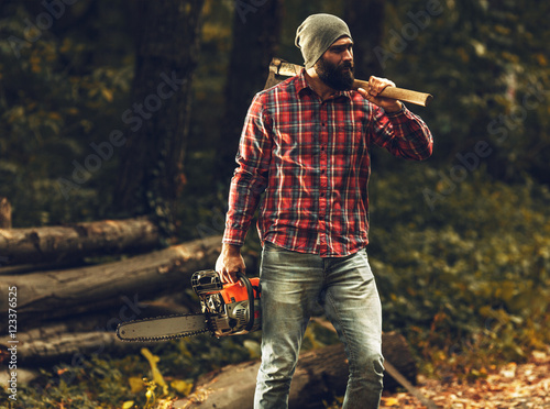 Lumberjack worker standing  in the forest with axe and chainsaw