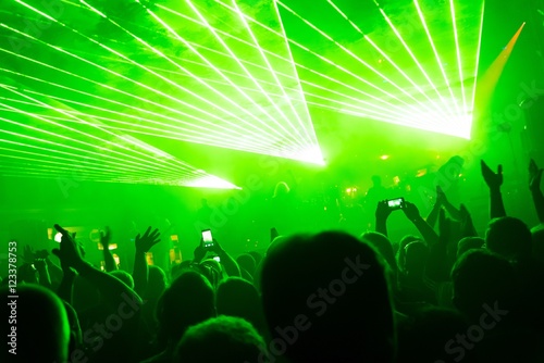 Rock concert, silhouettes of happy people raising up hands in front of bright, green stage laser lights. Space in top side.