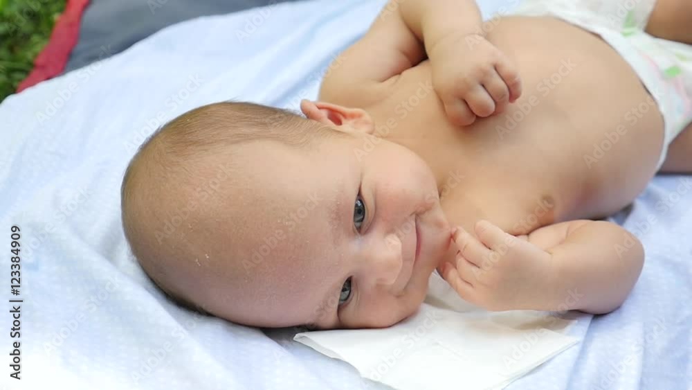 Cunningly smiling baby on a white sheet in a summer park. Handheld shot