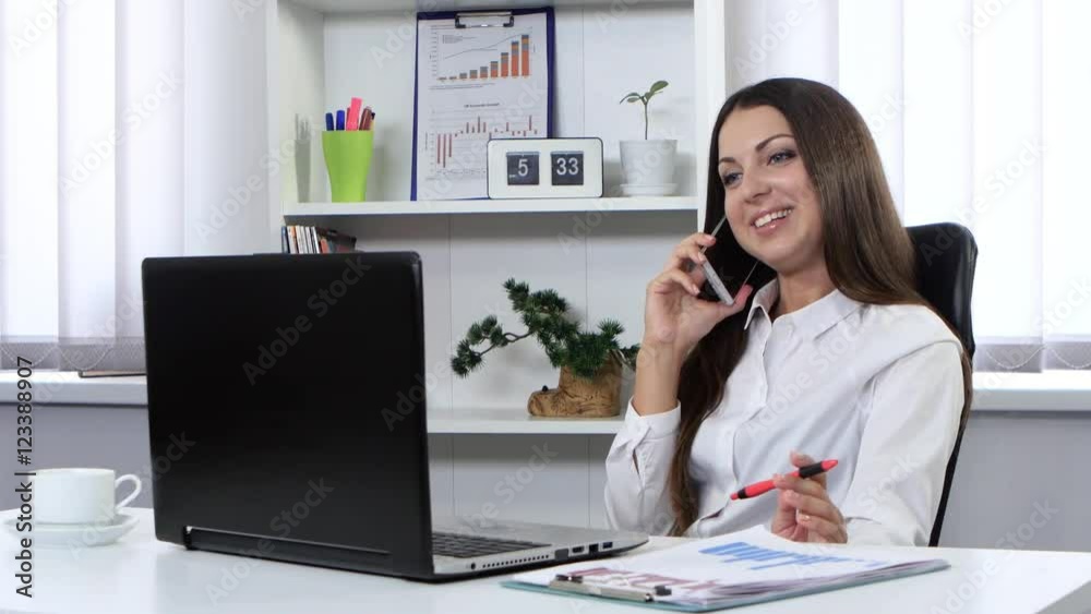 Girl is sitting in office and talking on the phone and holding in his hand a handle Girl is sitting in office and talking on the phone and holding in his hand a handle