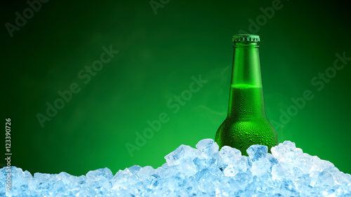 Bottle of cold beer in ice on green background