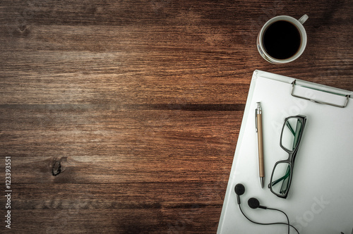 Coffee cup, glasses, pen, headphones and note on dark wood table