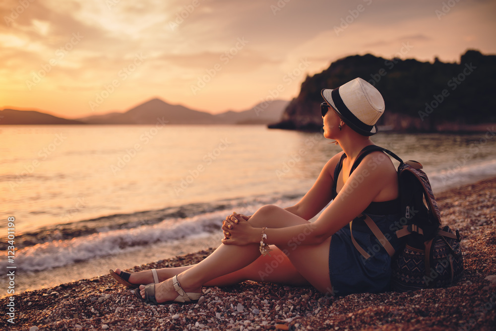 Woman sitting on pebble beach near sea at sunset
