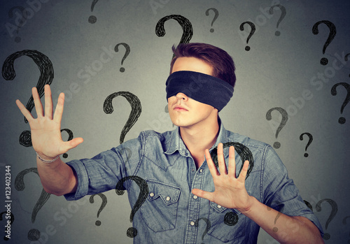 blindfolded man walking through many question marks photo