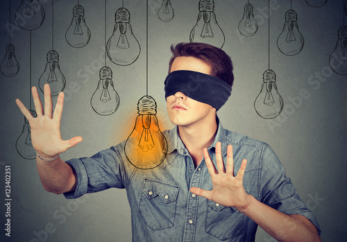 Blindfolded man walking through light bulbs searching for idea photo
