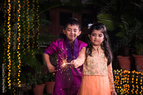 indian cute Boy and girl in traditional wear playing with sparklers or fulzadi or phuljhadi on diwali night