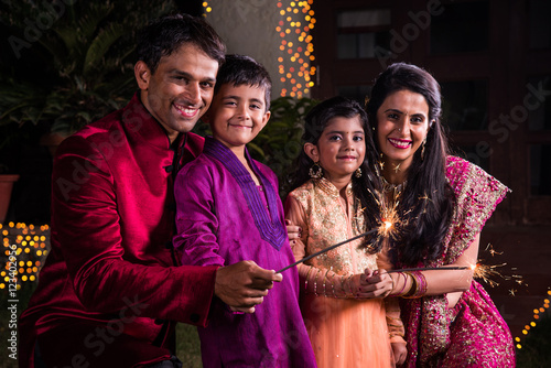 Indian Family in traditional wear playing with sparklers or phuljhadi while celebrating diwali festival, outdoor