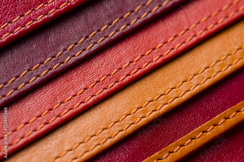 Leather samples with stitches, natural materials with seams of red, maroon, brown, orange colors and other warm shades, women's bag detail, macro shot, selective focus 