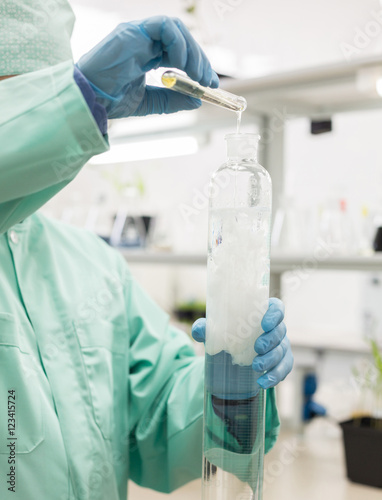 Lab technician pours liquid in high flask.