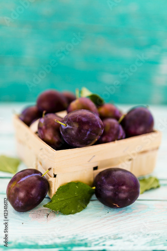 Ripe plums in a basket on a wooden table. Space for text. 