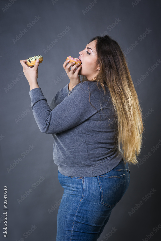 Beautiful young caucasian plus size model posing with donuts on a gray studio background Beautiful young caucasian plus size model posing with donuts on a gray studio background