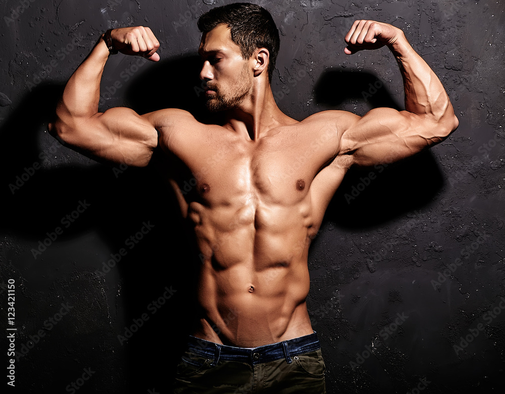 Portrait of strong healthy handsome Athletic Man Fitness Model posing near dark gray wall