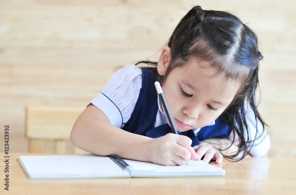 little girl writeng the notebook with pencil on the table school uniform little girl writeng the notebook with pencil on the table school uniform