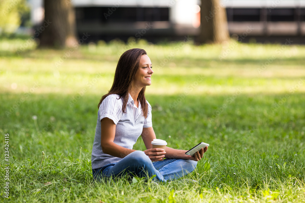 Obraz premium Beautiful businesswoman is drinking coffee and using digital tablet while resting from work at the park.